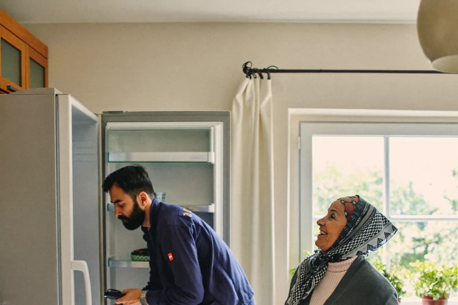 Mutfakta açık Ariston buzdolabının soğutma arızasını tespit ederek onarım yapan servis teknisyeni, ev sahibi yanında bekliyor